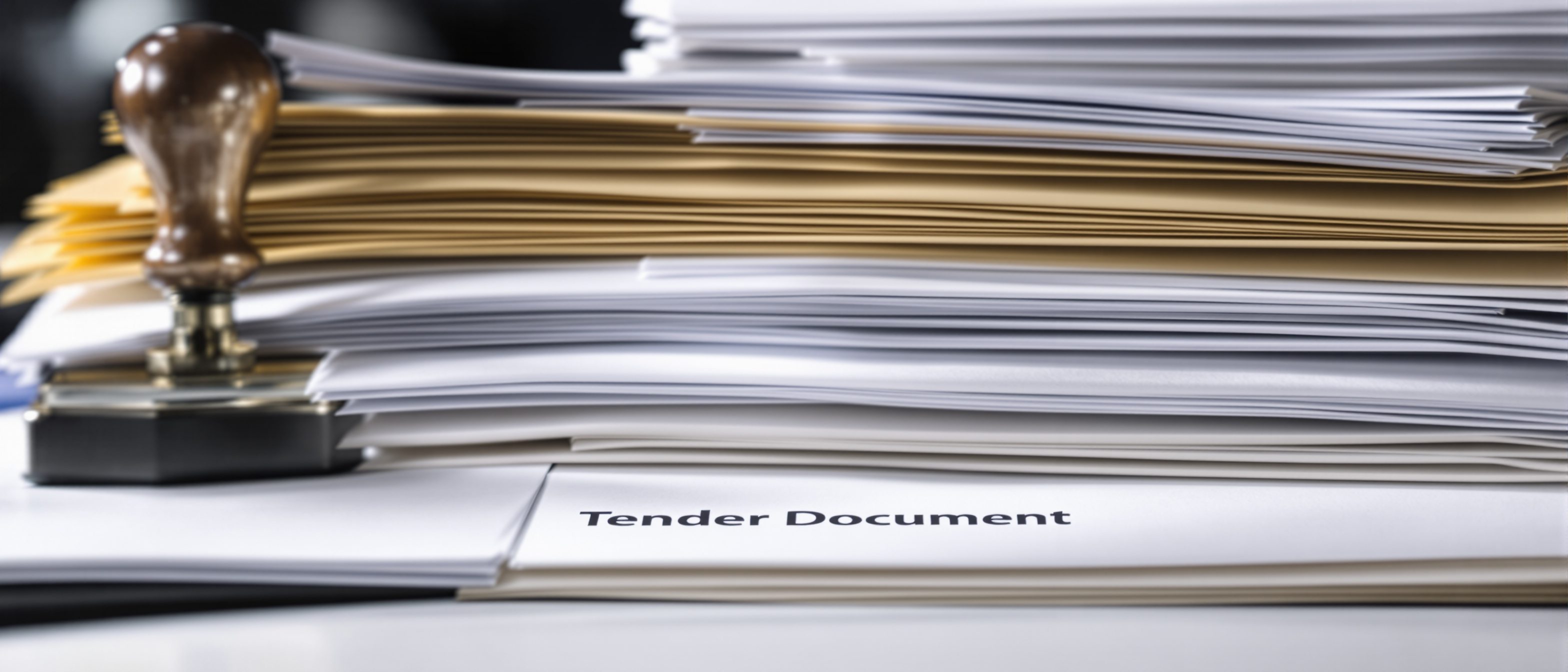 A stack of sealed tender documents and bound bid books with an official stamp — the disciplined, auditable competitive selection of a contractor.