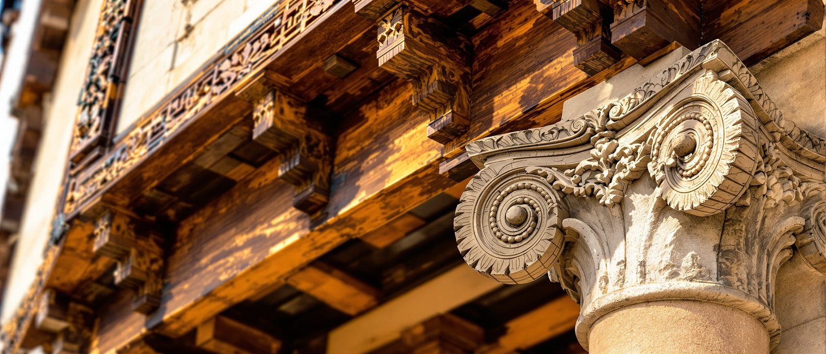 A close-up of a traditional carved timber bracket and stone column capital on an old building, showing material and craft in warm daylight, documentary, no legible text