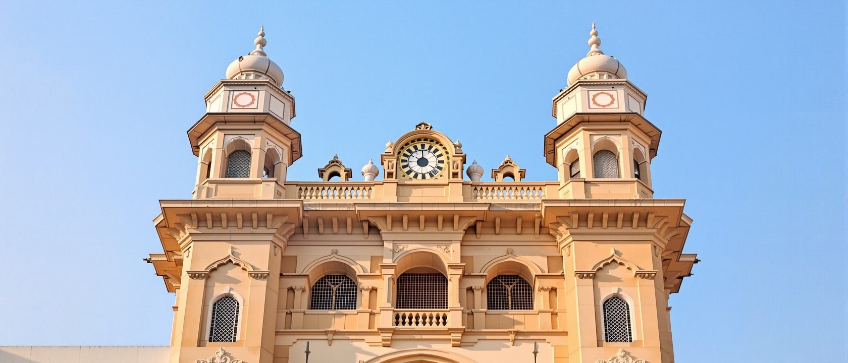The ornate facade of a historic Indian building showing a distinct architectural style with arches, brackets and carved detail, warm daylight, documentary, no legible text