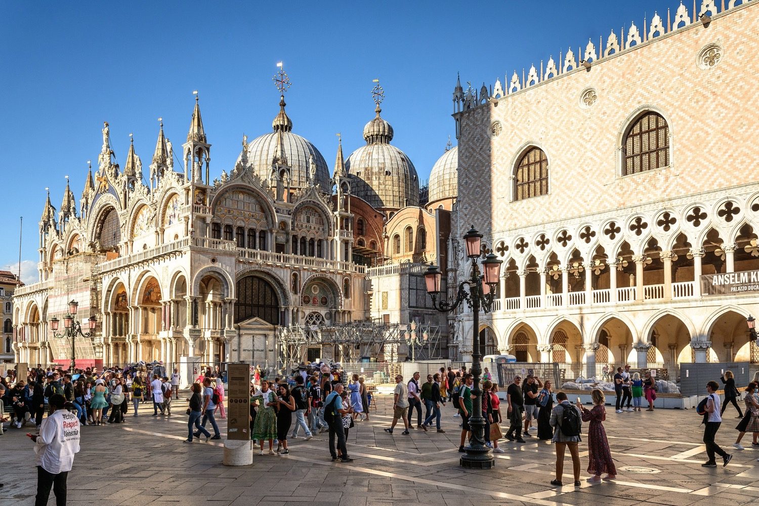 The Doge's Palace (Palazzo Ducale, right) beside St Mark's Basilica, Venice — Venetian Gothic loggias of pointed, quatrefoil-traced arches under a pink-and-white patterned wall.