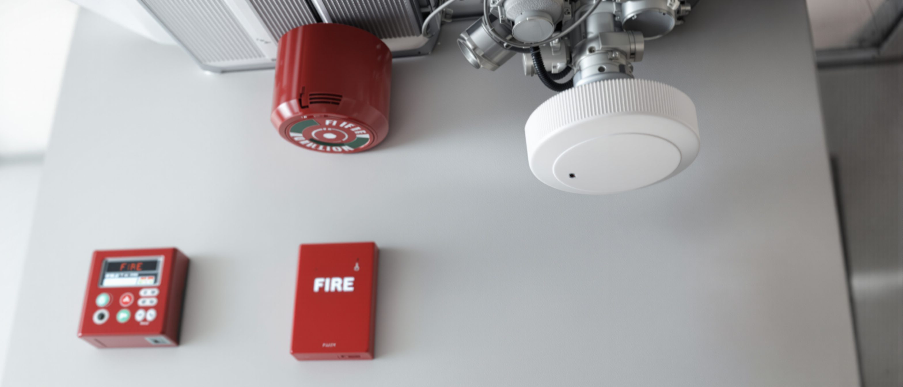 A close view of a red fire alarm control panel and a ceiling fire sprinkler head and smoke detector in a modern building, the active fire-detection and suppression systems.