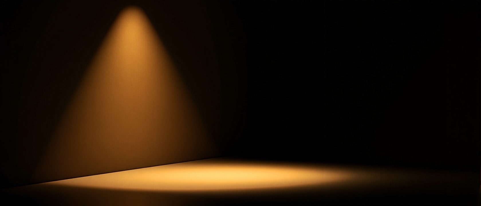 A dramatic retail display where a single hero product glows under a tight accent spotlight against a deliberately darker surround, warm focused pool of light, rich shadow, jewellery-case theatre, no text