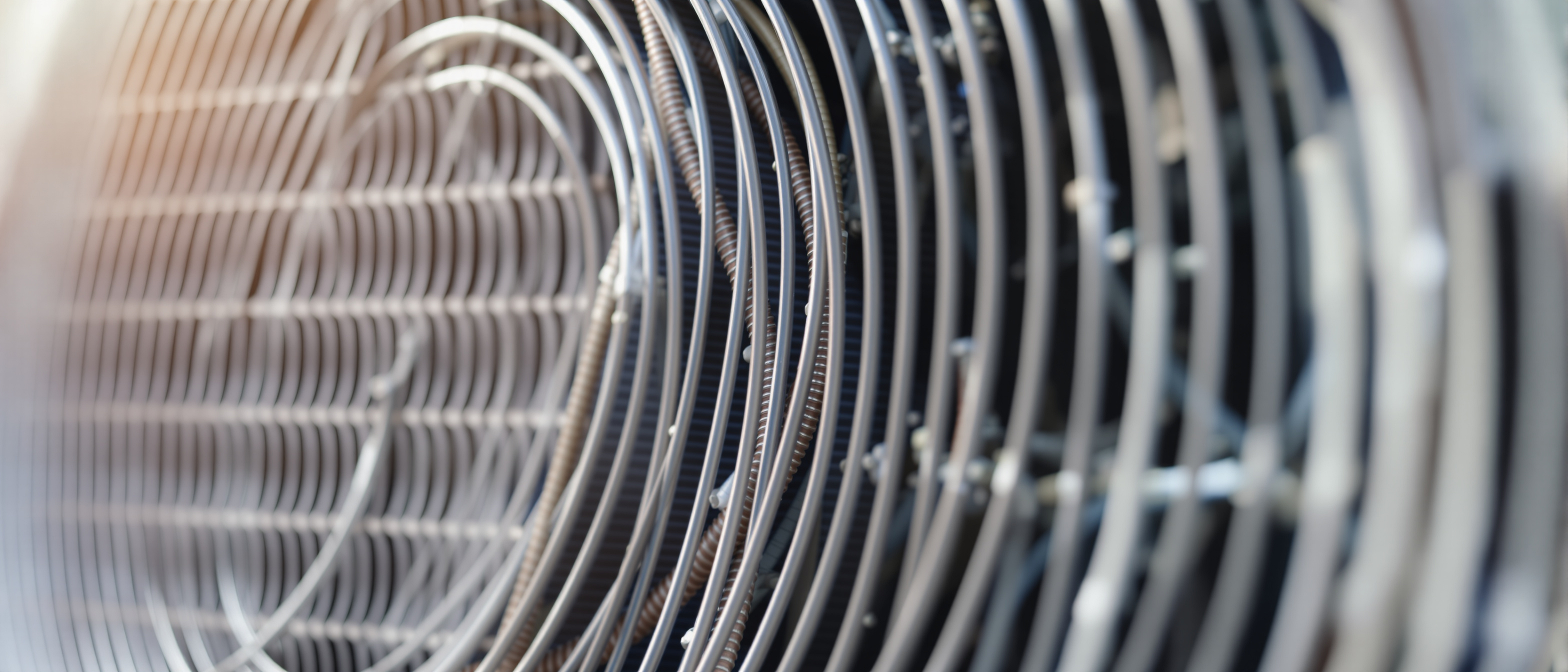 The finned coil and copper pipework of an air-conditioning outdoor unit in clean daylight, close and technical, no text