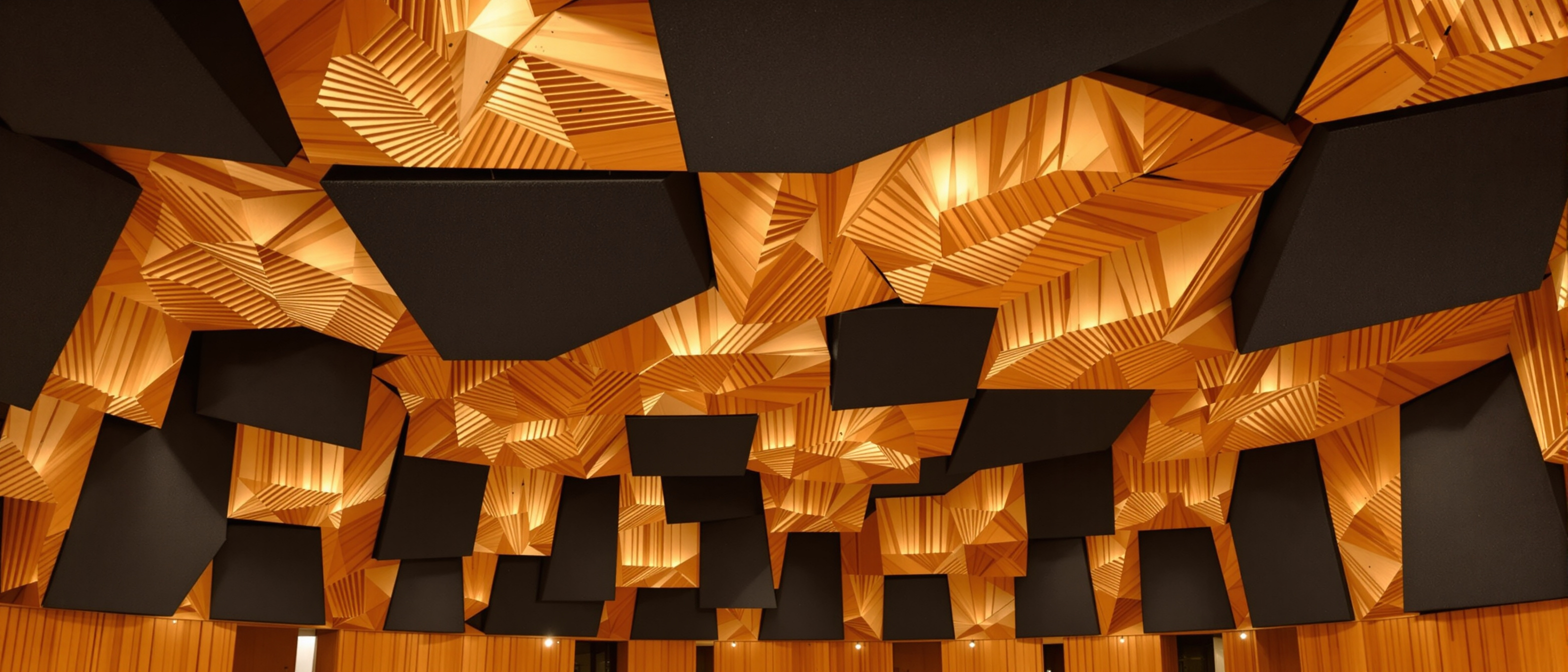 An auditorium ceiling and walls lined with sculpted acoustic panels and diffusers in warm light, geometric and technical, no text