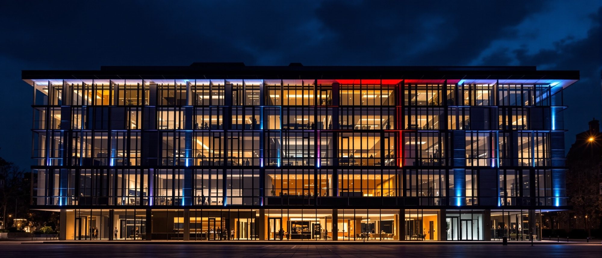 A contemporary building façade lit at night — warm and cool architectural lighting picking out its form against a dark sky, the exterior layer of the craft.