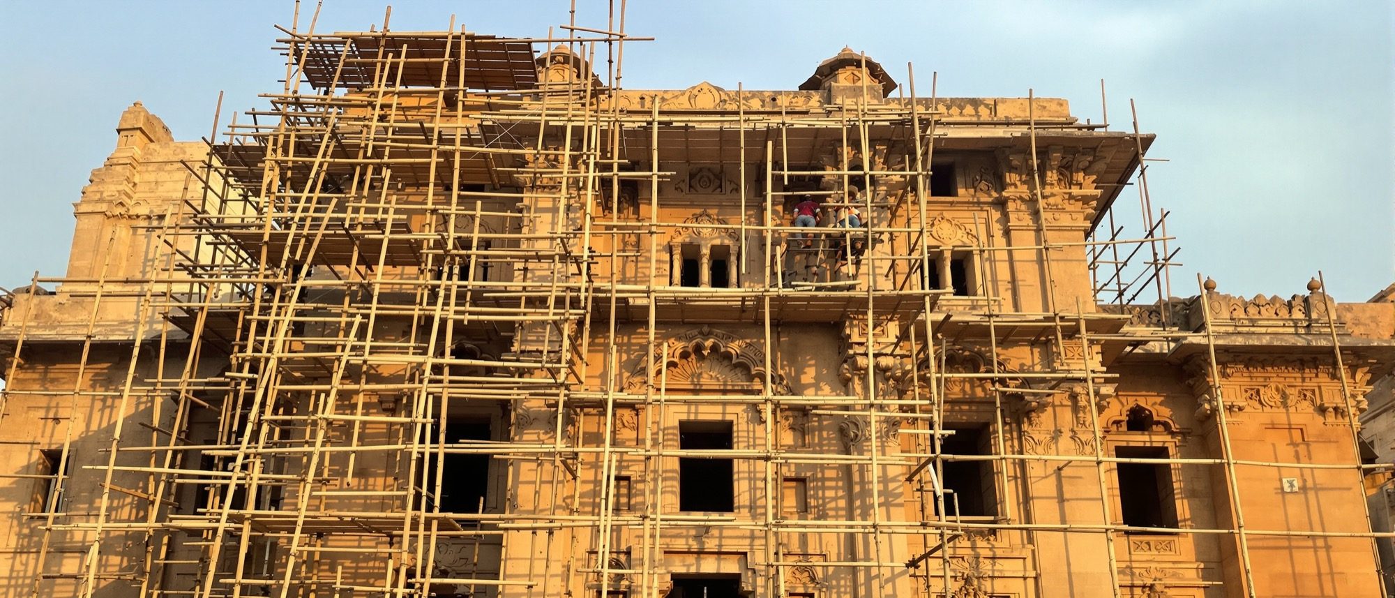A heritage stone building under conservation — scaffolding and conservators repairing carved stone with traditional materials, a careful hand on the past.