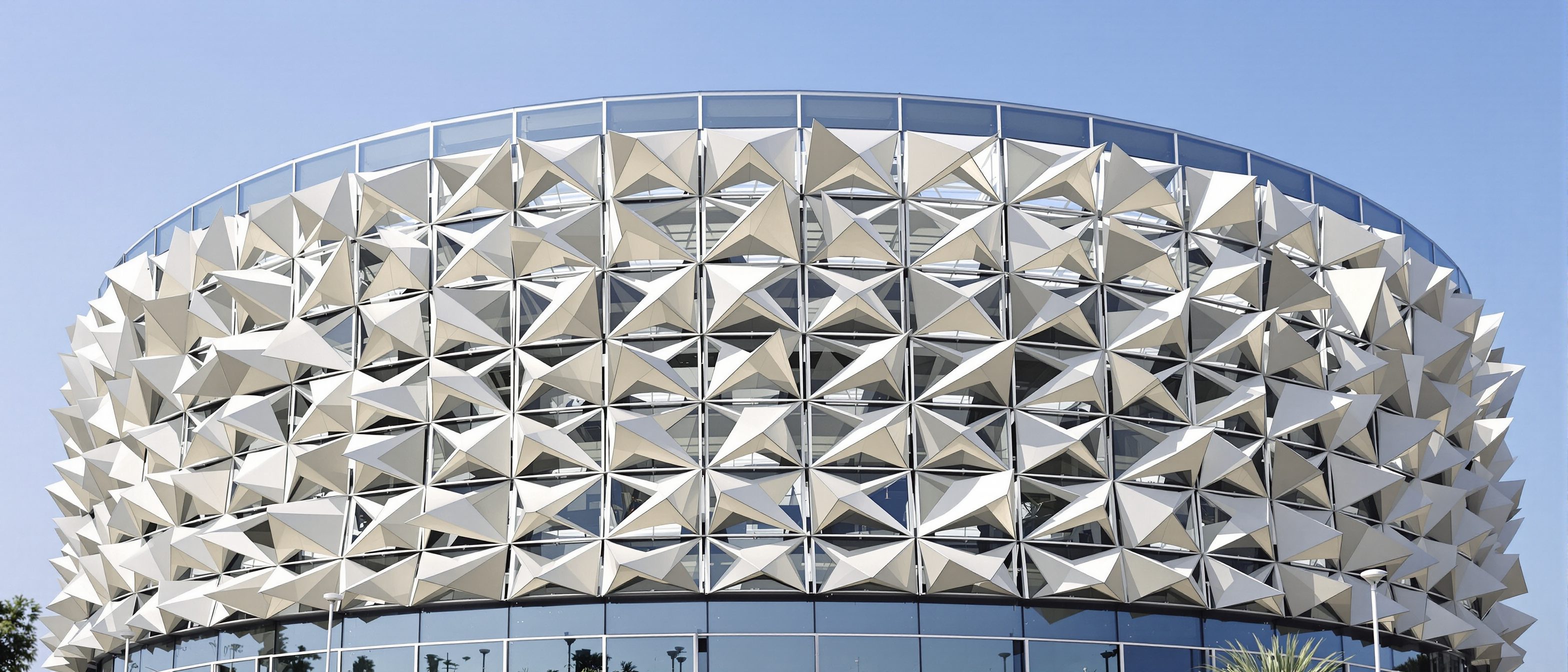 A dynamic responsive building facade of folding triangular shading panels in a hot climate — a computer-controlled mashrabiya-like screen, some panels open and some folded shut to track the sun, under a bright sky.