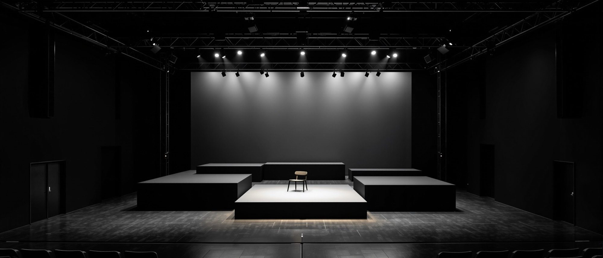 A black-box theatre with a minimal set and an exposed lighting rig — the flexible stage where the actor–audience relationship is reinvented each show.