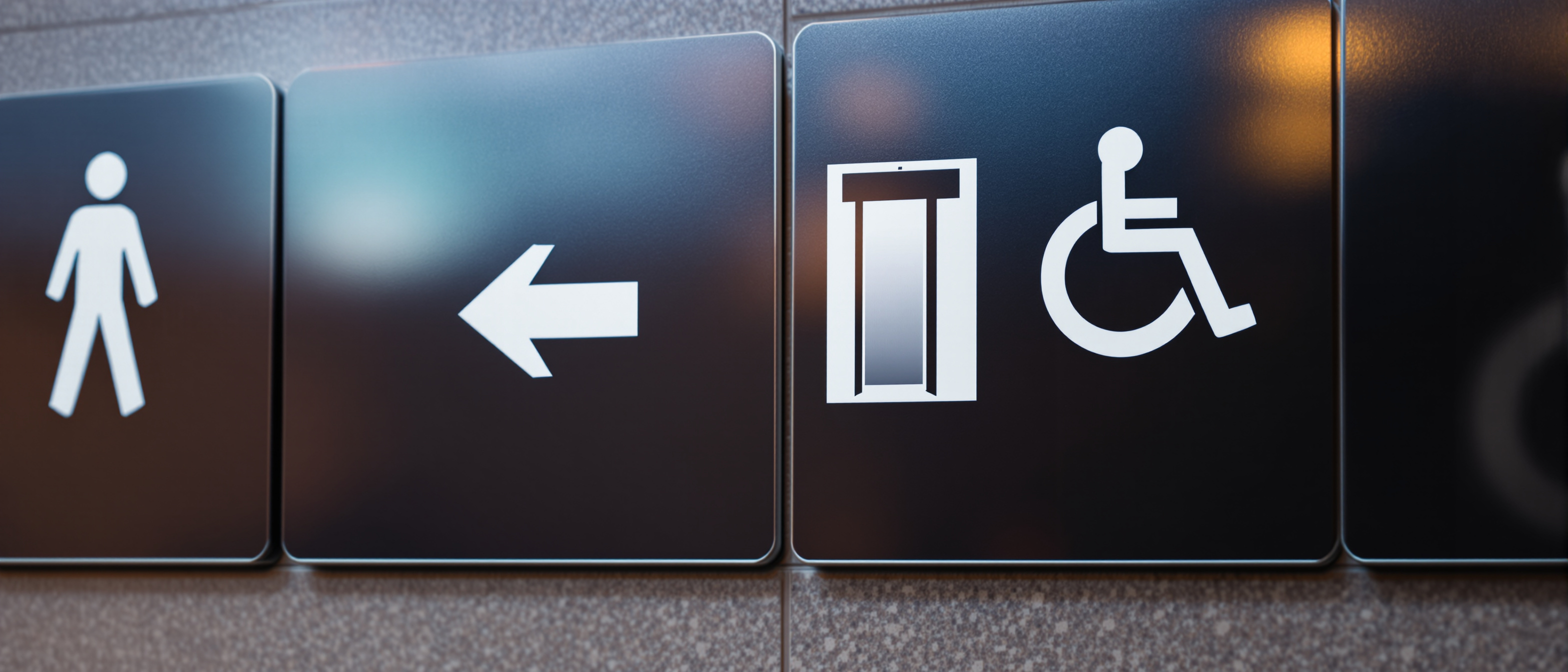 A coordinated wall of room-identification and directional signage in one consistent graphic system with blank panels and standard pictograms, warm daylight, clean and graphic, no legible text