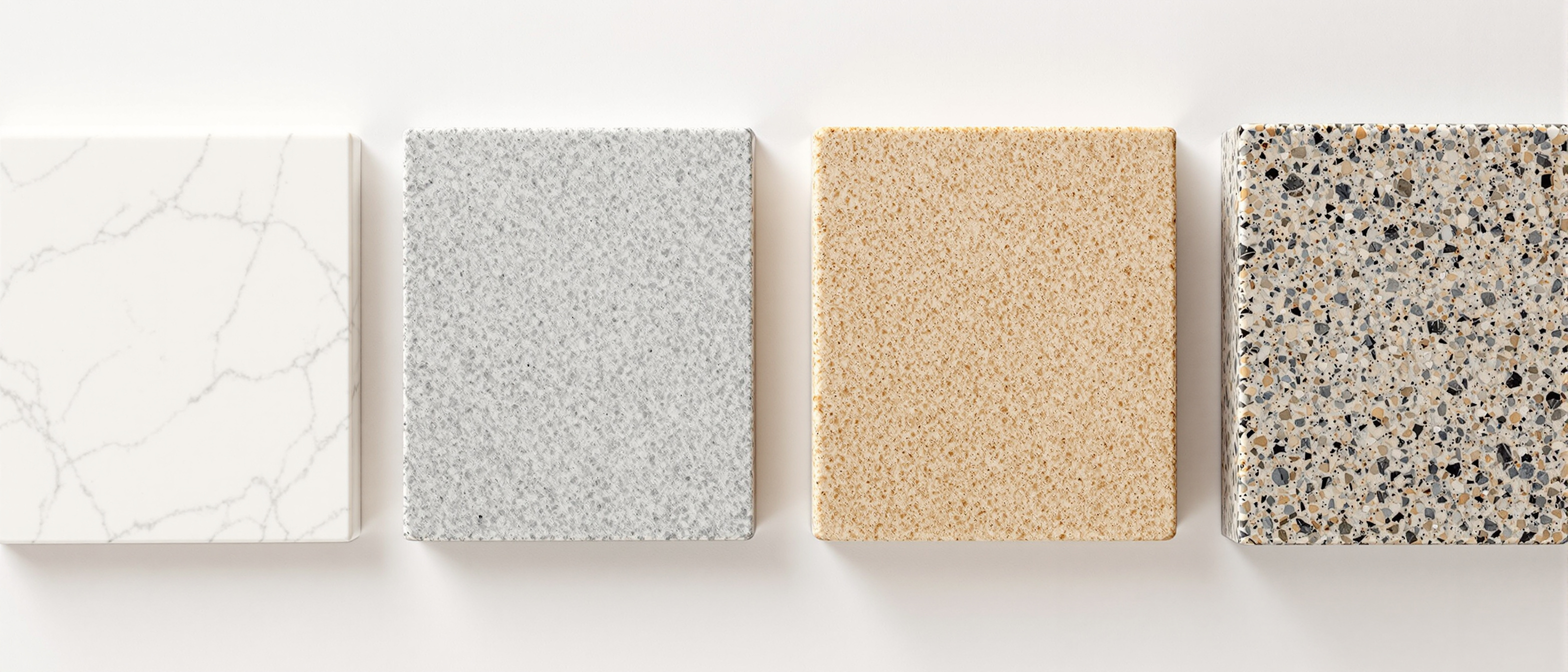 A flat-lay of natural stone samples on a workbench — a polished white marble offcut, a blue-grey Kota tile, a warm sandstone piece and a speckled granite block, in soft daylight